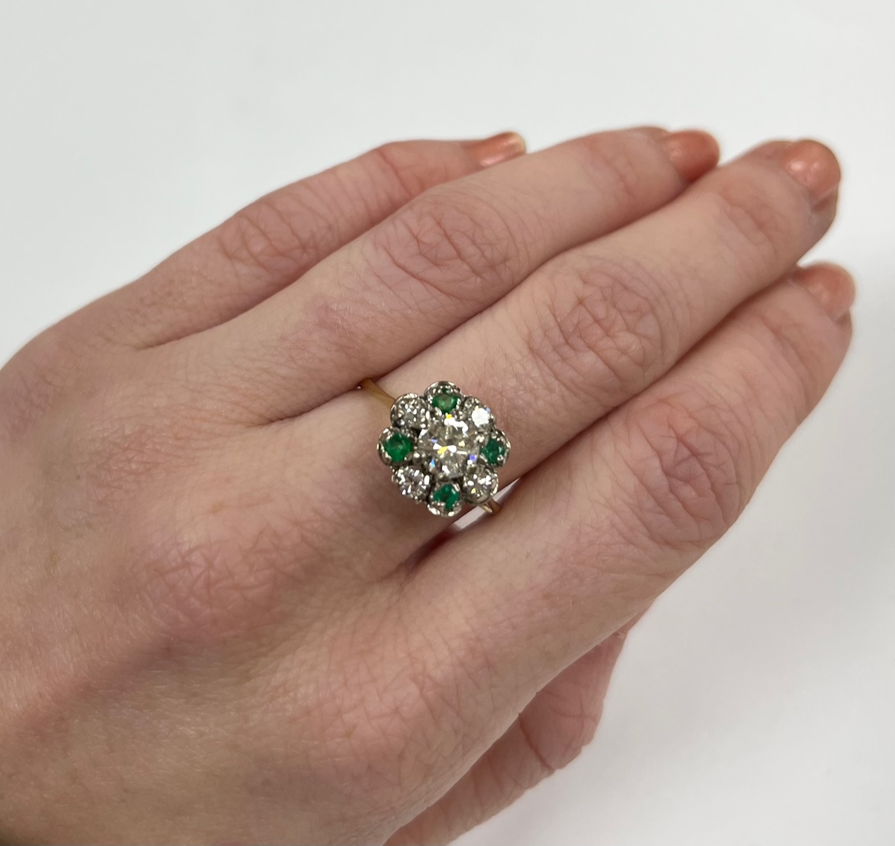 A yellow metal, diamond and emerald set flower head cluster ring, size P, gross weight 4 grams, the central diamond measuring approximately 5.5mm in diameter.
